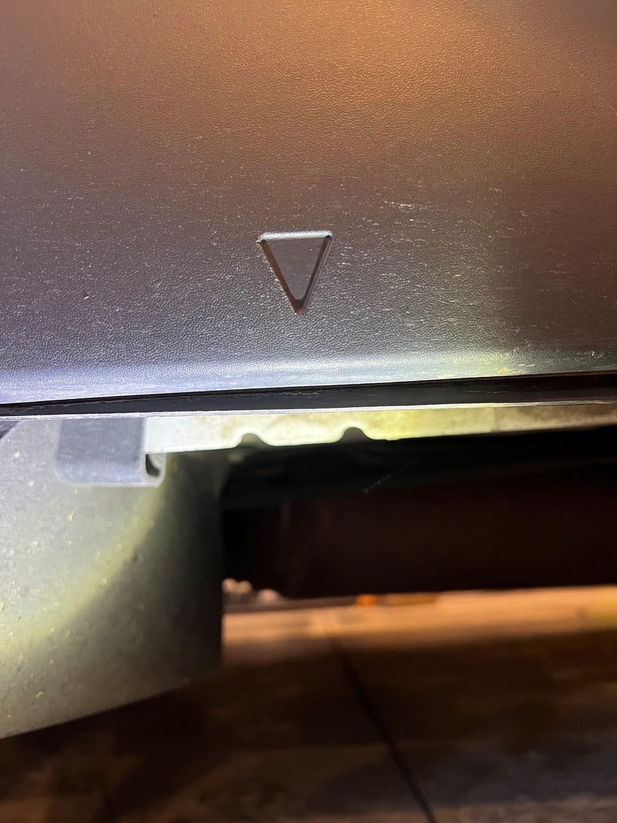Look for the triangle molded into the side cladding — the two notches in the pinch weld sit right below it.